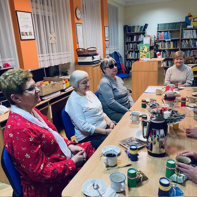 Uczestniczki spotkania siedzą przy stole ustrojonym świątecznymi dekoracjami i rozmawiają o przeczytanej książce. 