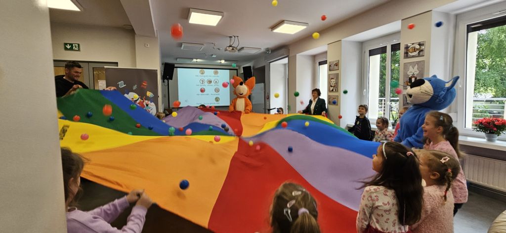 Dzieci podrzucają piłeczki wspólnie podnosząc chustę.