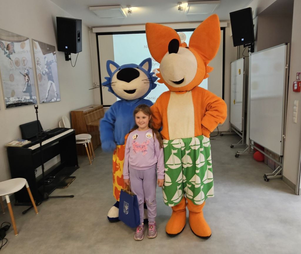 Uśmiechnięta dziewczynka w towarzystwie liska Fenka i kotka Maksia prezentuje swój dyplom za zajęcia I miejsca w konkursie. 