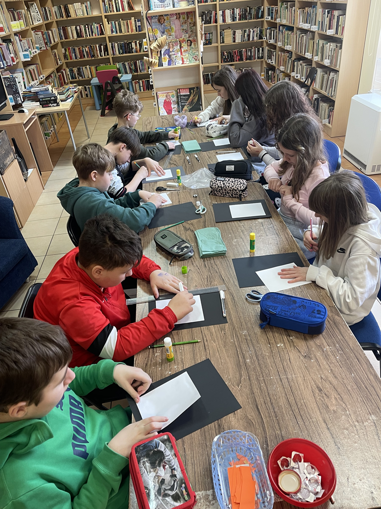 Dziesiątka uczni&oacute;w siedzi przy podłużnym stole i pochyleni pracują nad swoimi dziełami.