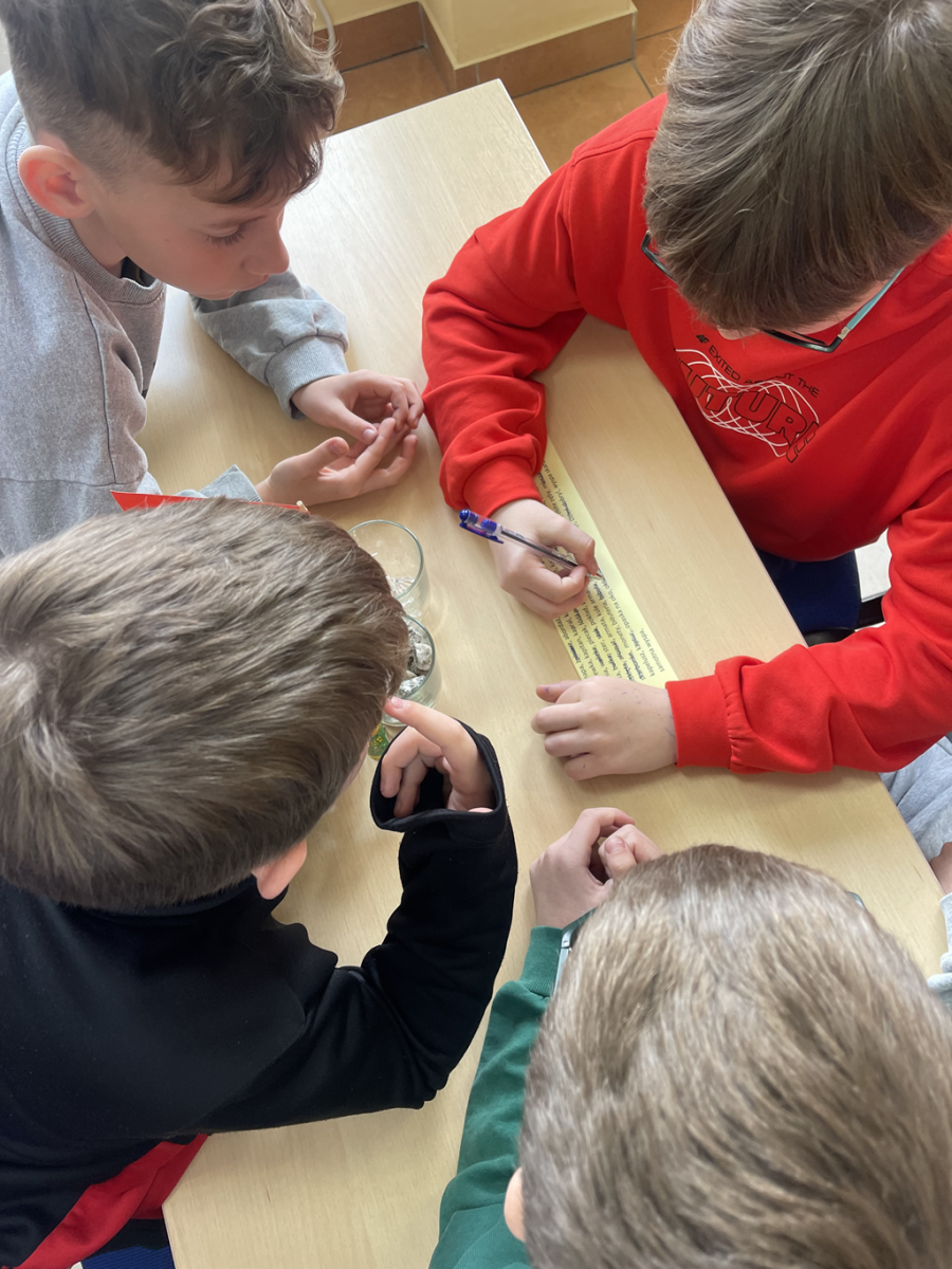 Czterej chłopcy, siedzący przy stoliku rozwiązują kolejne zadanie: wykreślankę słowną. 