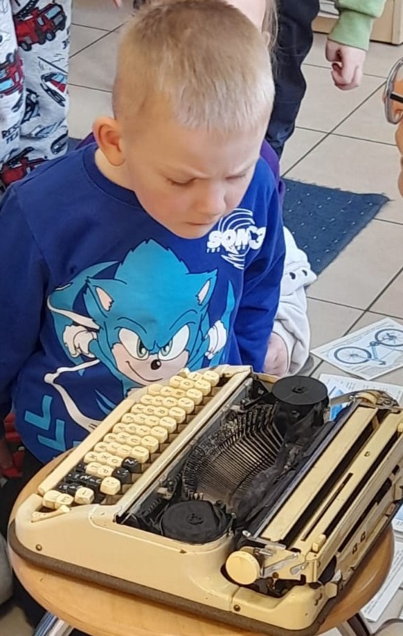 Chłopczyk pochylony nad maszyną do pisania, z zainteresowaniem przypatruje się jej wnętrzu.