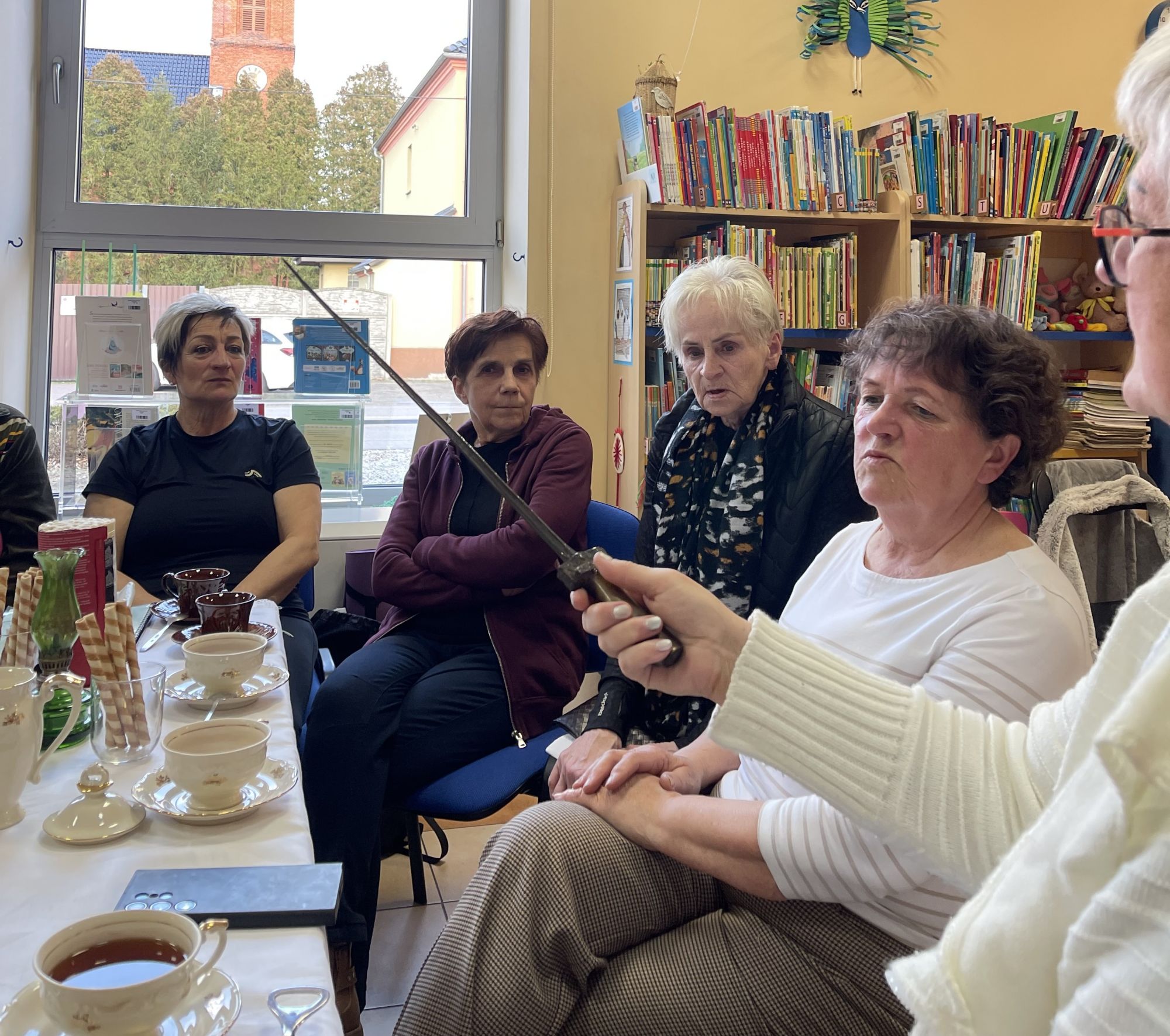 Pięć pań przygląda się bagnetowi, kt&oacute;ry unosi jedna z kobiet.