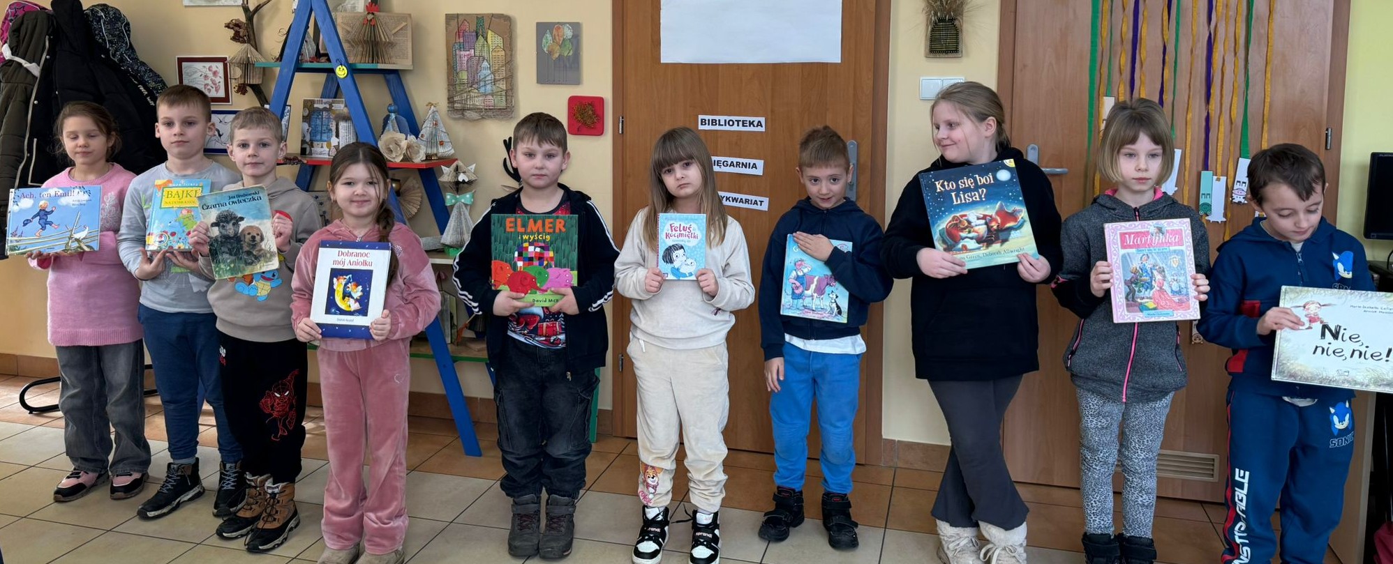 Dziesięcioro uczni&oacute;w, trzymając w dłoniach książkę  stoi w rzędzie w tytułowym porządku alfabetycznym.