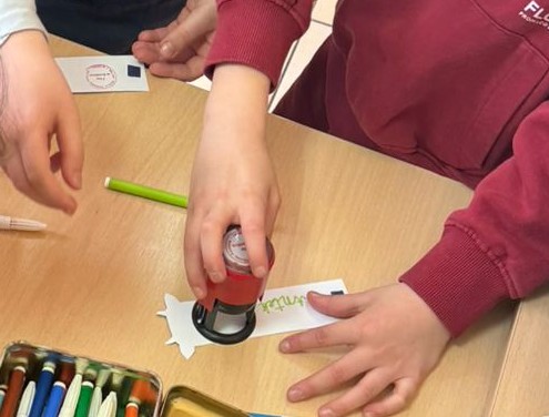 Zbliżenie na dziecięce ręce, w kt&oacute;rych trzymana jest pieczątka biblioteki.