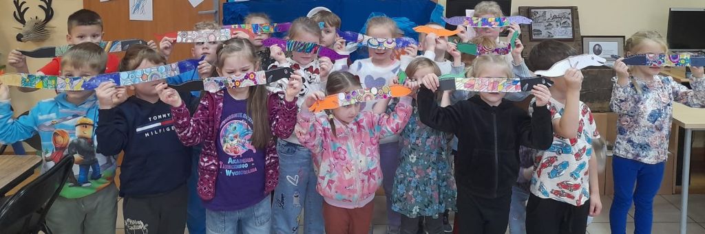 Dzieci, stojąc w rzędach, demonstrują przed sobą papierowe węgorze.