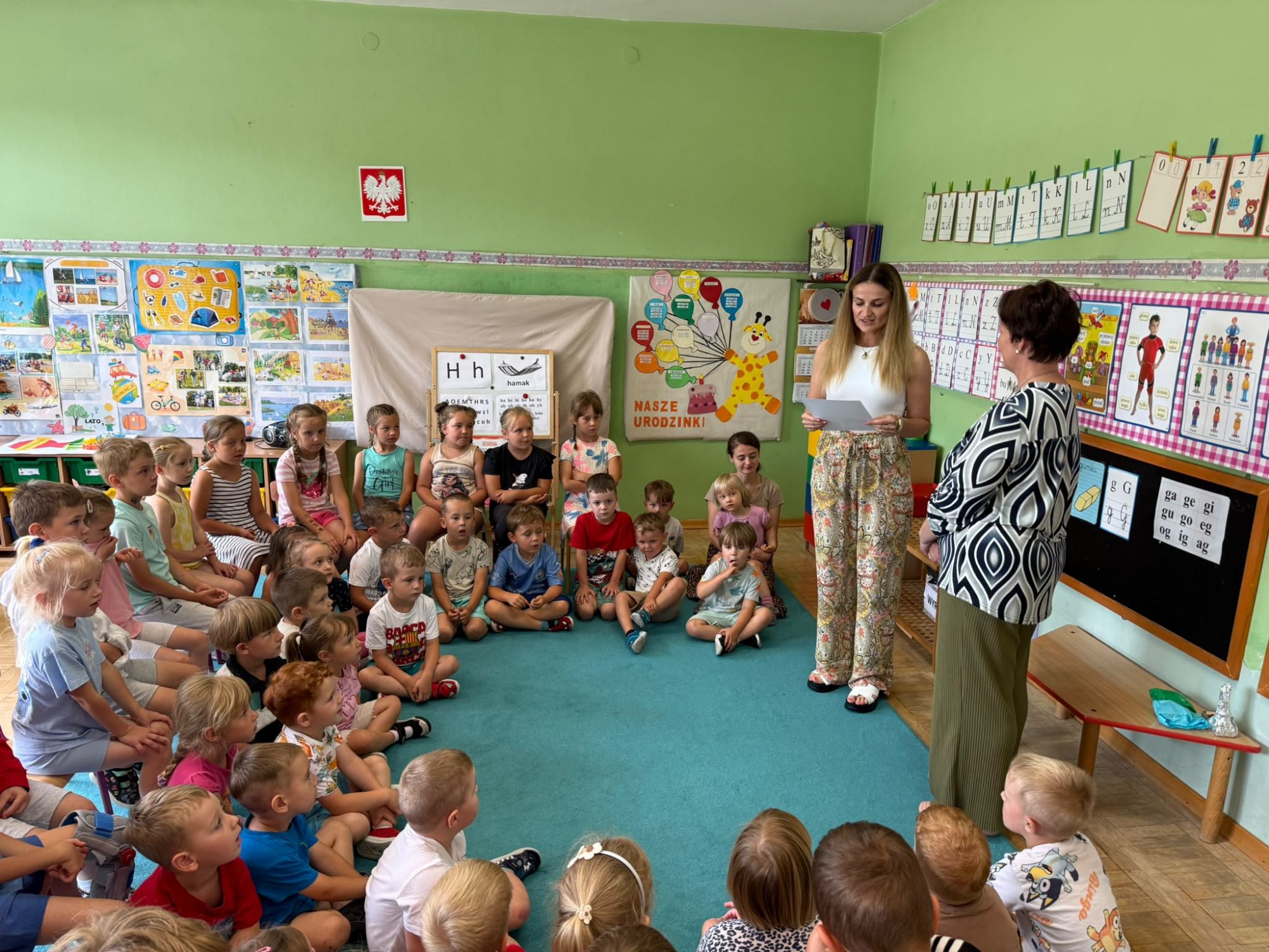 Pani nauczycielka z przedszkola czyta treść podziękowań dla bibliotekarki przy grupie przedszkolak&oacute;w.