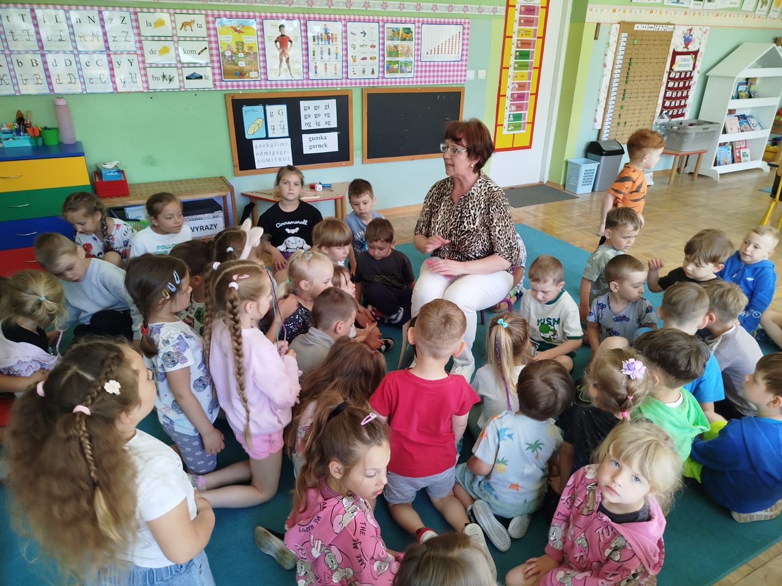 Bibliotekarka siedzi na krzesełku otoczona dziećmi i prowadzi dyskuje na temat rodziny i domu.