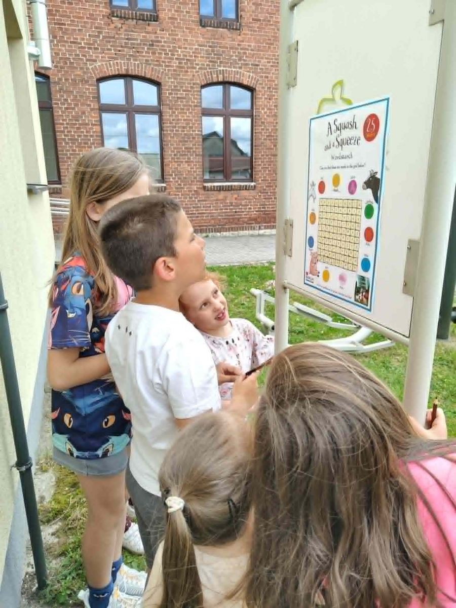  stojąca grupa dzieci rozwiązuje naklejoną na słupek ogłoszeniowy kartę pracy