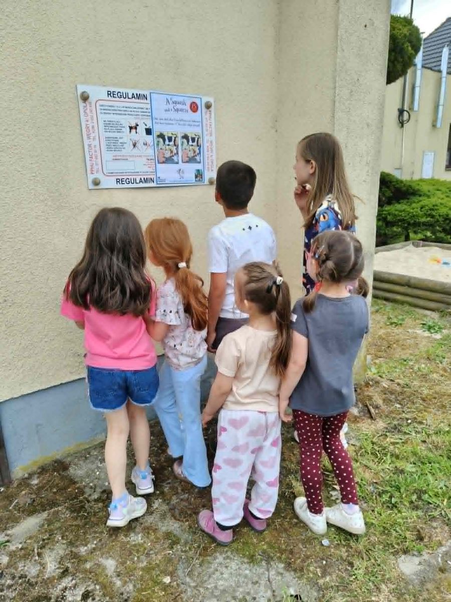 ) stojąca grupa dzieci rozwiązuje naklejoną na planszę ogłoszeniową kartę pracy