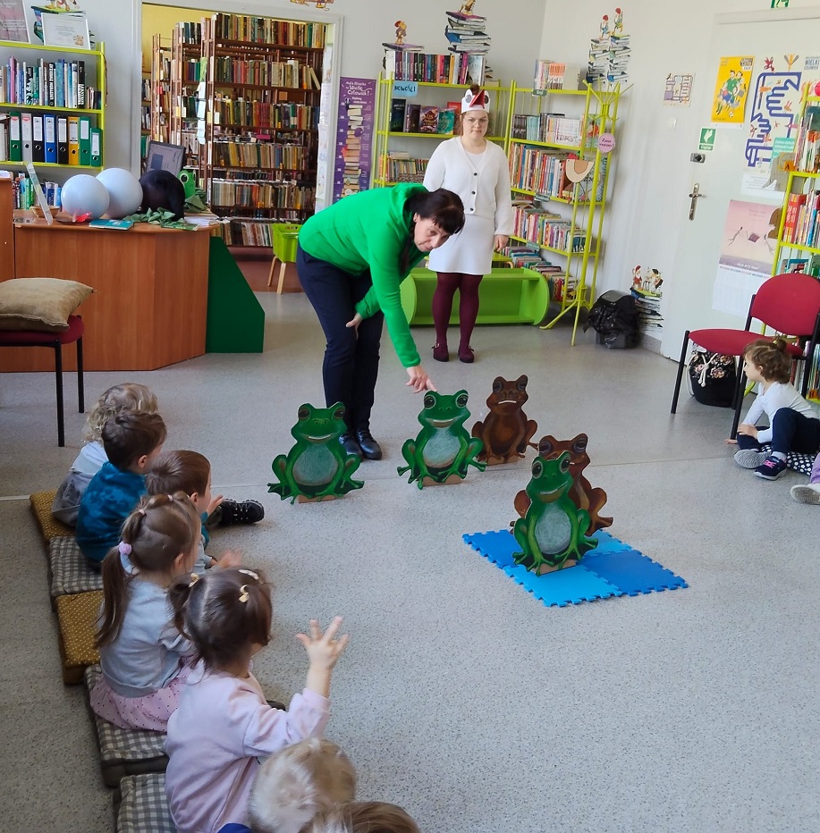 Pani wskazuje na żabki postawione na podłodze i prosi dzieci by razem z nią liczyły ile ich jest.