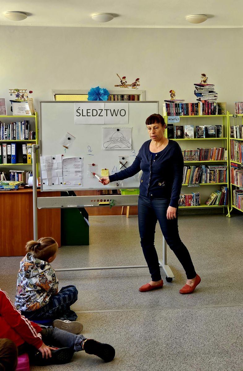 Pani bibliotekarka podsumowuje zebrane przez dzieci dowody na tablicy.