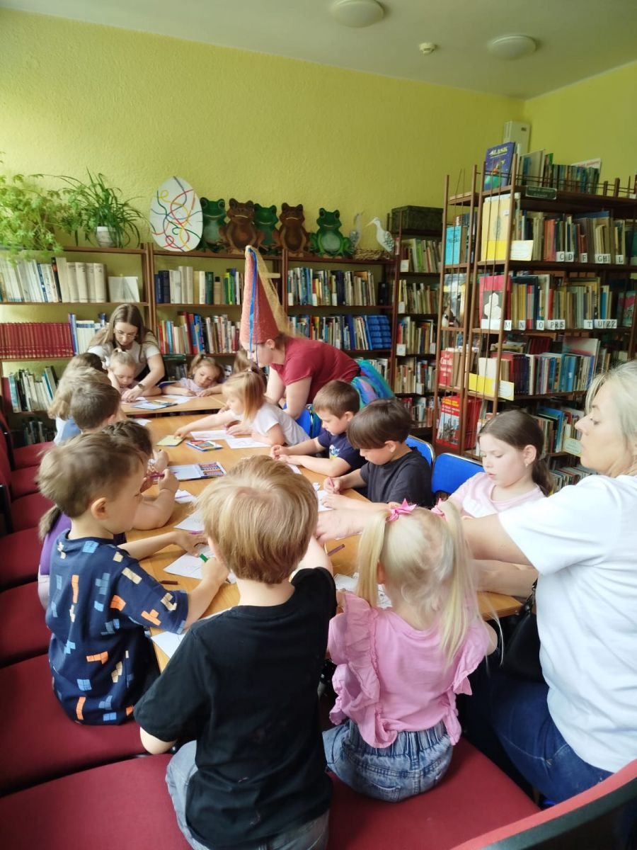 Grupa dzieci siedzi przy stole i wykonuje pracę plastyczną.