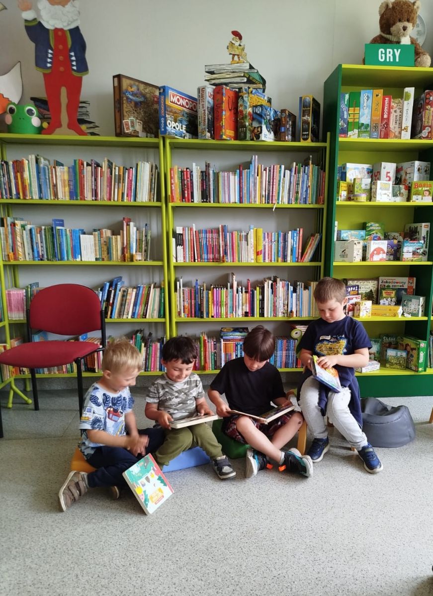 Grupa chłopc&oacute;w przegląda książeczki, kt&oacute;e można wypożyczać w bibliotece.
