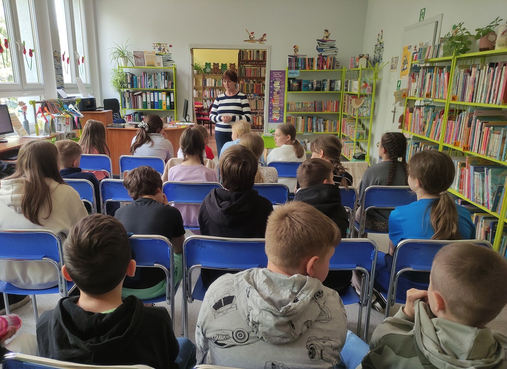 Bibliotekarka przekazuje najważniejsze informacje o funkcjonowaniu biblioteki stojąc przed grupą uczni&oacute;w.