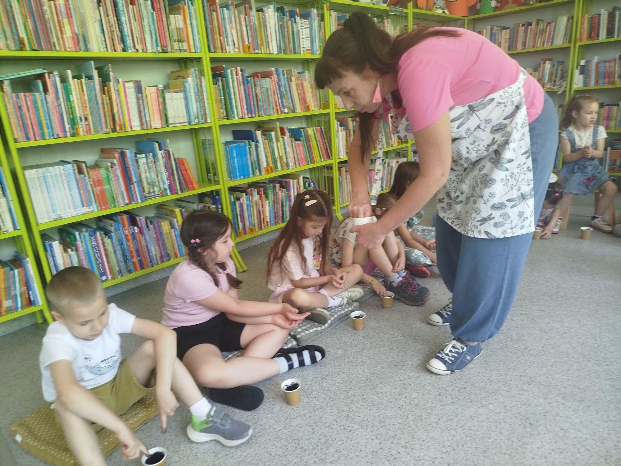 Bibliotekarka rozdaje dzieciom kubeczki z ziemią i nasionka, by dzieci mogły je zasadzić.