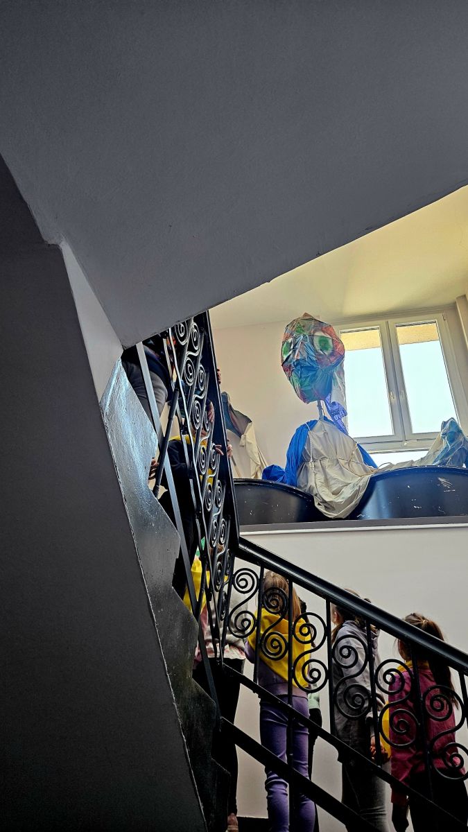 Grupa dzieci na schodach patrzy na dużą lalkę teatralną