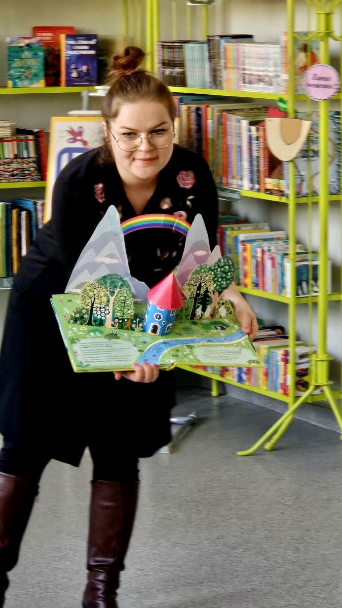 Młoda bibliotekarka pokazuje dzieciom książkę przestrzenną z serii o Muminkach