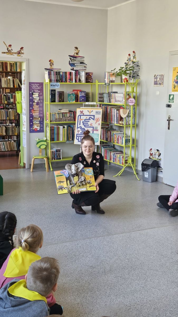 Młoda bibliotekarka pokazuje dzieciom książkę przestrzenną o zwierzętach