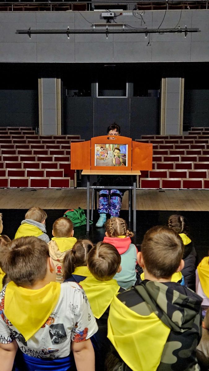 Dzieci słuchają historii przedstawionej w japońskim drewnianym teatrzyku kamishibai