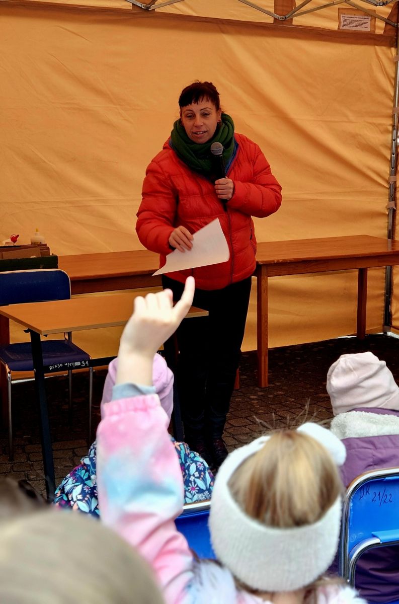 Bibliotekarka stoi przed grupą dzieci i zadaje im pytania