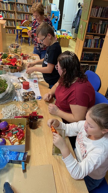 Uczestnicy warsztat&oacute;w siedzą przy stole i wykonują ozdoby świąteczne