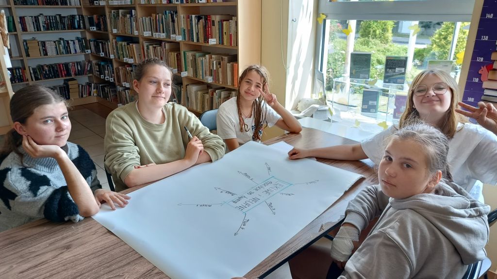 Uczestniczki zajęć siedzą przy stole i wykonują ćwiczenie