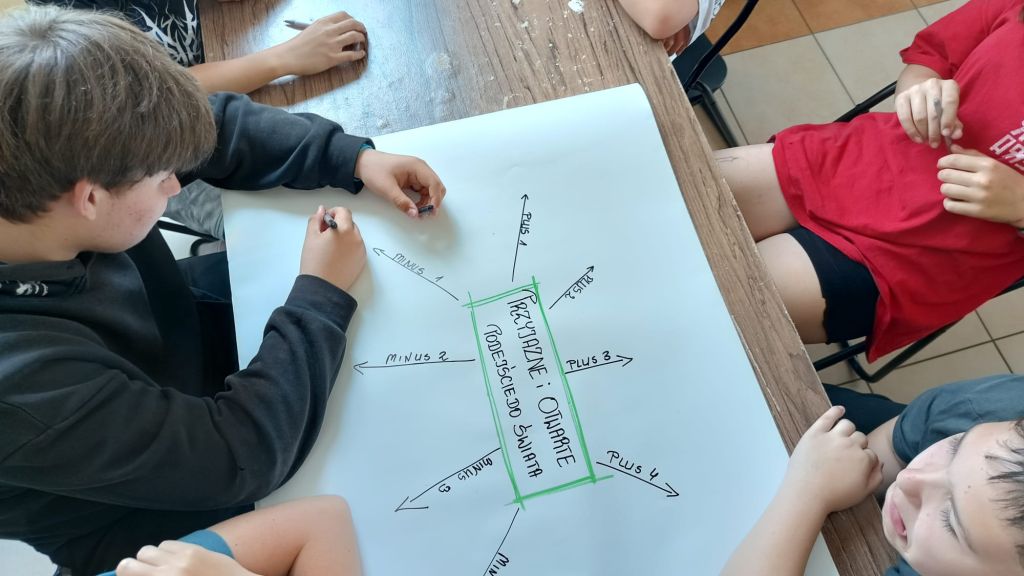 Uczestnicy zajęć siedzą przy stole i wykonują ćwiczenie