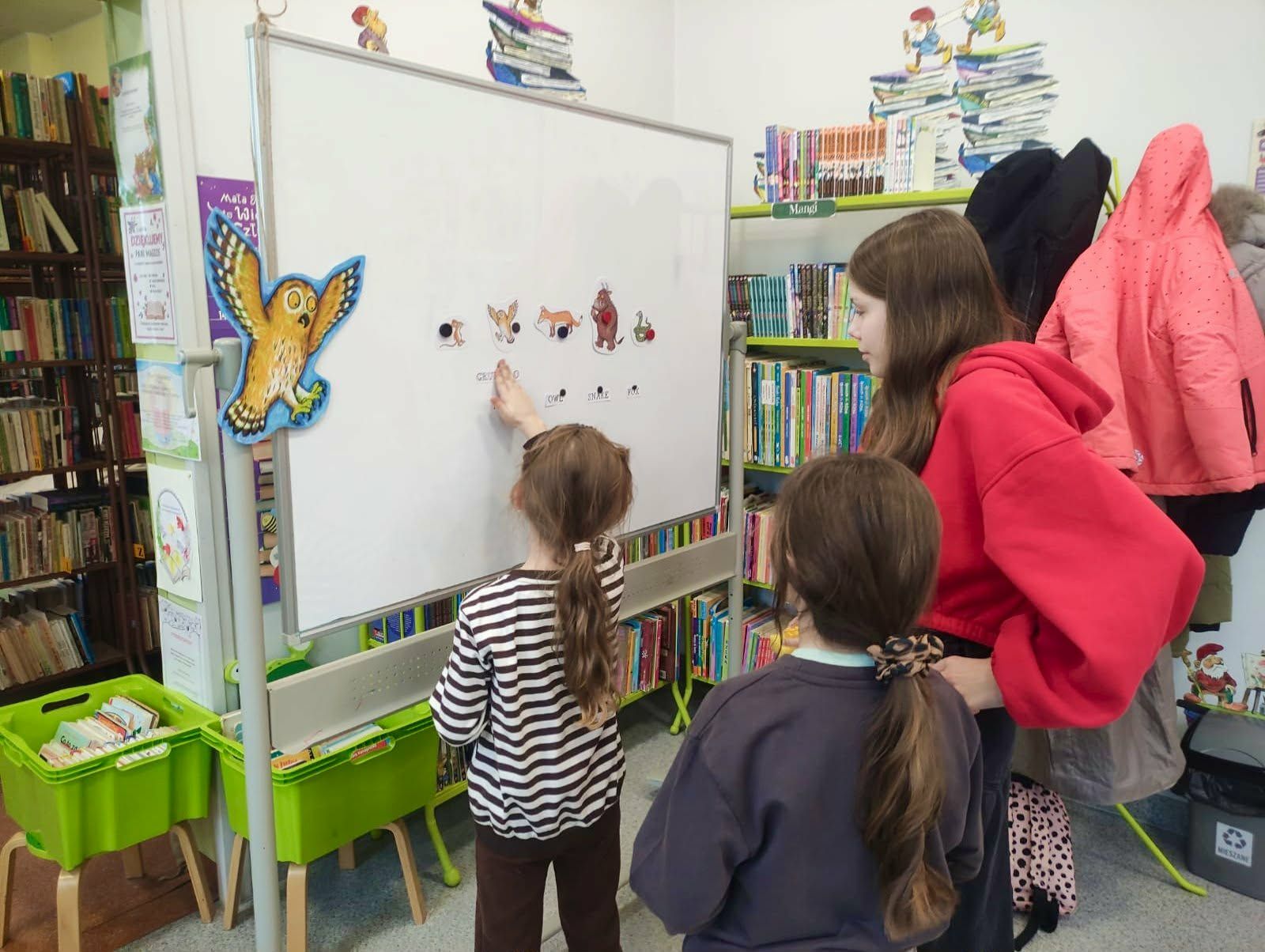 Grupa trzech dziewczynek rozwiązuje zadanie obrazkowe stojąc przy białej tablicy.