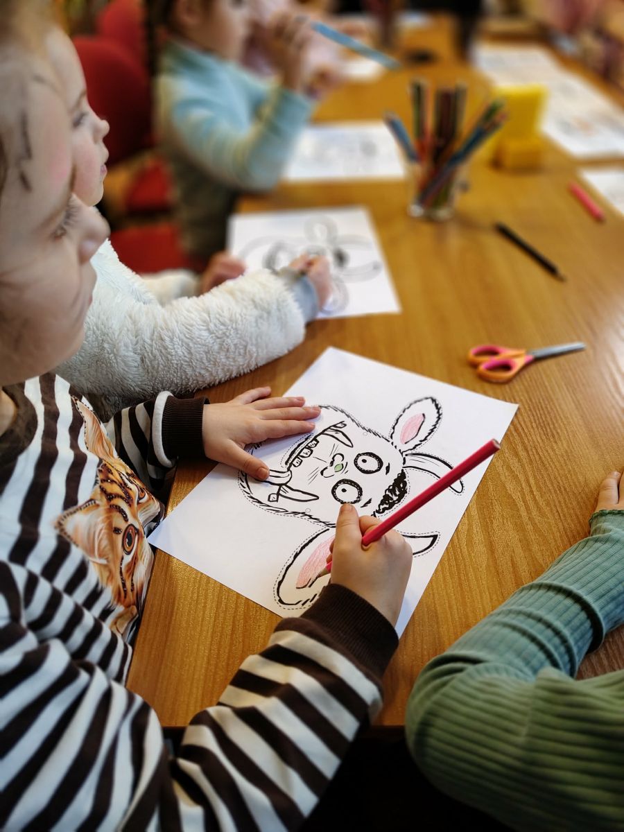 Dziecko koloruje kredkami leżącą na stole kartkę z maską Gruffalo.